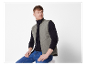 Ein Mann trägt eine graue gesteppte Weste und eine dunkelblaue Jeans.