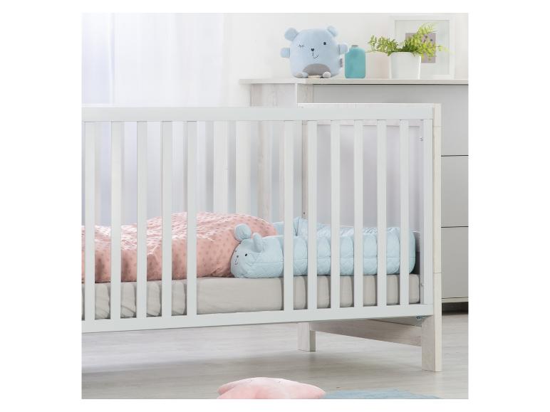 Weißes Babybett mit rosa und blauer Bettwäsche, mit Plüschtieren.