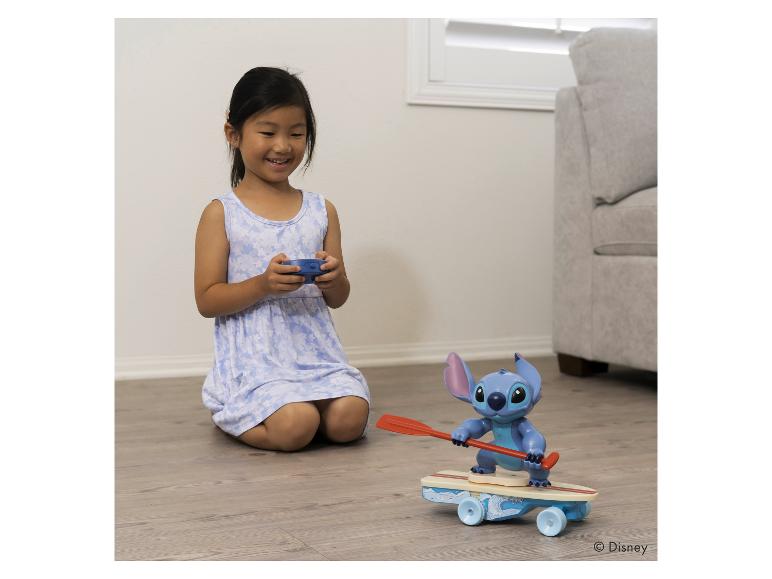 Ein junges Mädchen lächelt, während es ein ferngesteuertes Stitch-Spielzeug auf einem Skateboard steuert.
