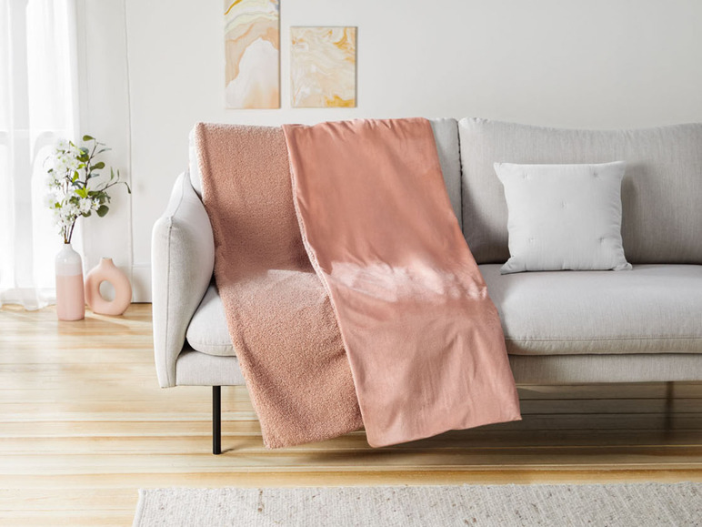 Zwei weiche Decken in Rosatönen auf einer grauen Couch.