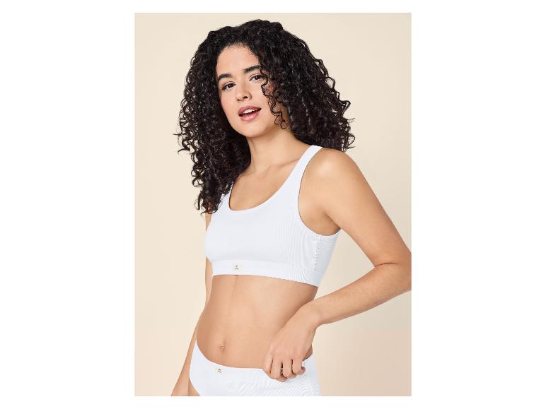 Frau mit lockigem Haar trägt einen weißen gerippten Bralette und passende Slips.
