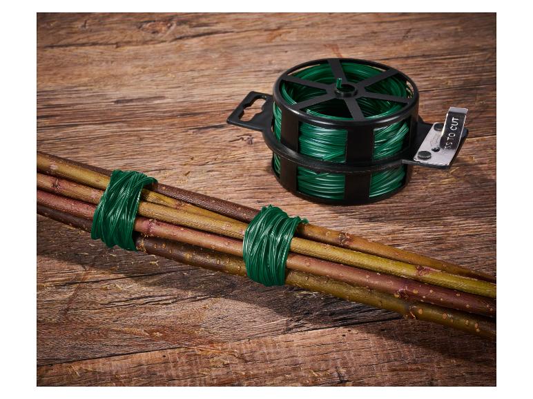 Grüner Gartendraht im Spender mit Schneider und damit gebundenes Bündel Äste auf Holzuntergrund.
