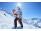 Frau in Skijacke und Skihose steht mit einem Snowboard im Schnee.