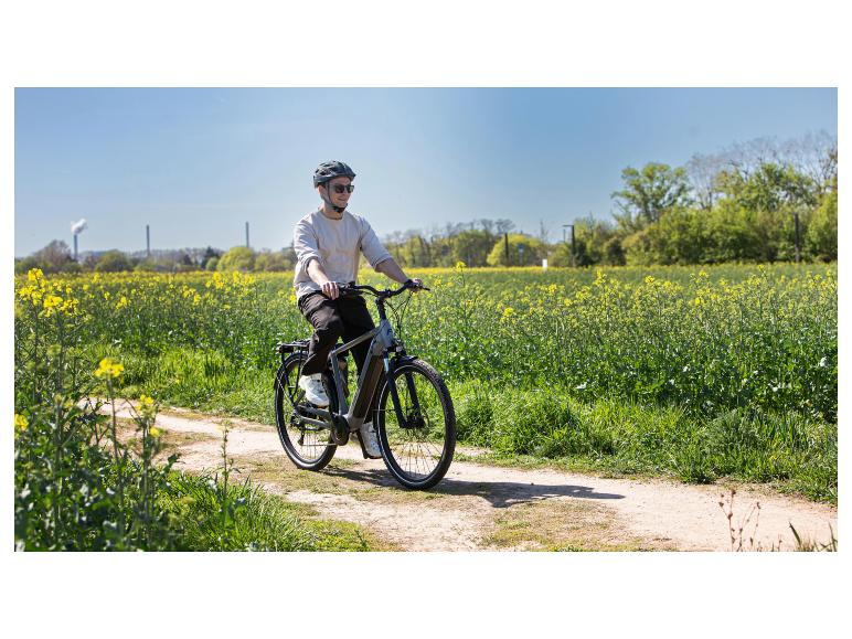 Mann auf E-Bike auf einem Feldweg neben einem Rapsfeld.
