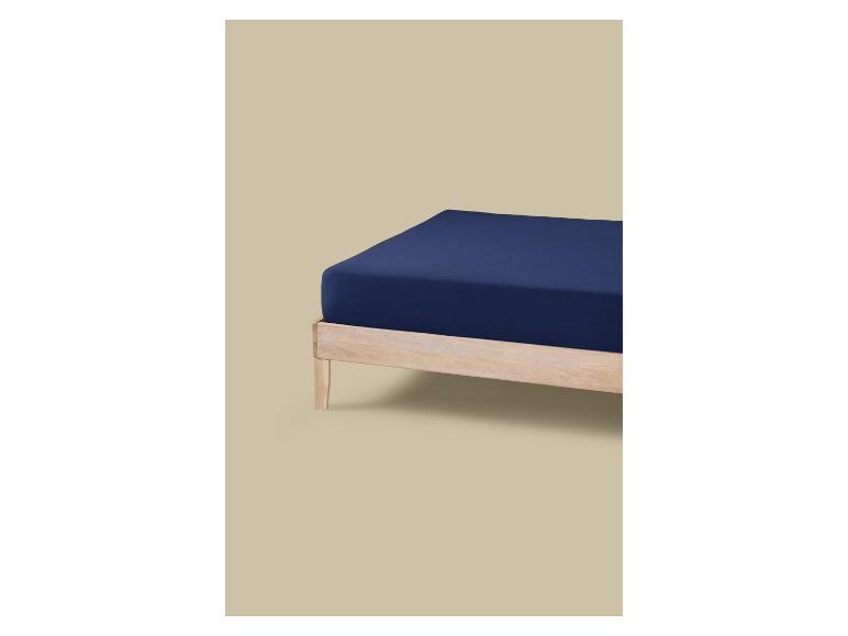 Ein Bett mit hellem Holzrahmen und einer Matratze, die mit einem dunkelblauen Spannbettlaken bezogen ist.