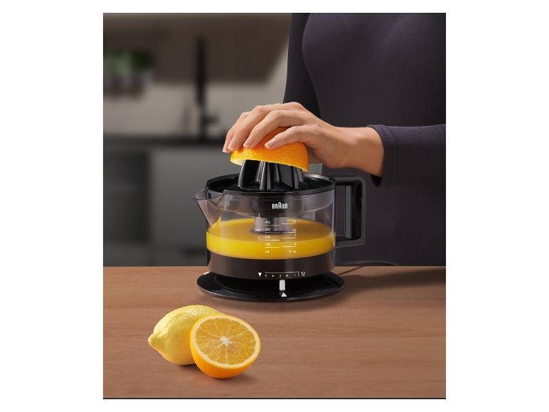 Frau presst eine Orange mit einer Zitruspresse, mit Zitronen und Orangen auf einem Holztisch.