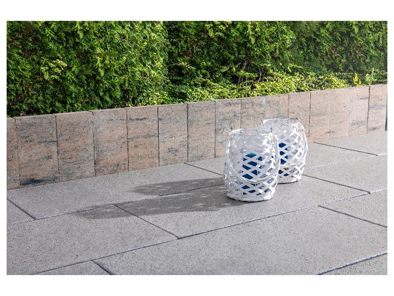 Zwei weiße Laternen auf einer gepflasterten Terrasse mit einer grünen Hecke im Hintergrund.