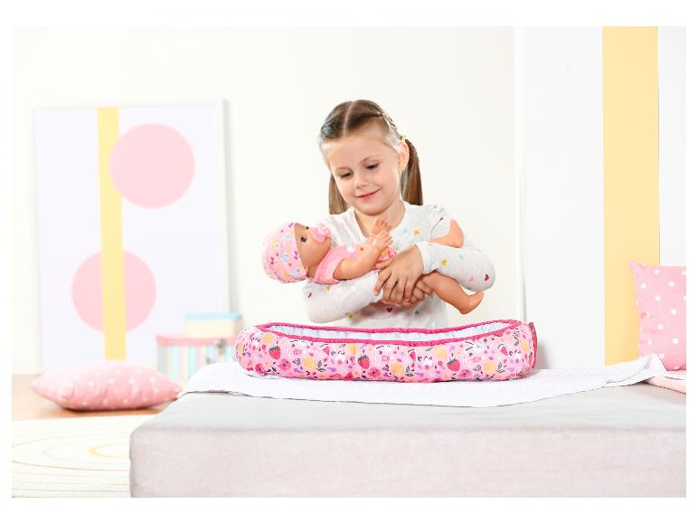 Mädchen hält eine Puppe mit Schnuller und ein Puppenbett mit Fruchtmotiv.