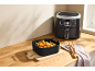 Schwarze Silikonform für Heißluftfritteuse mit Essen auf einem Holzbrett.