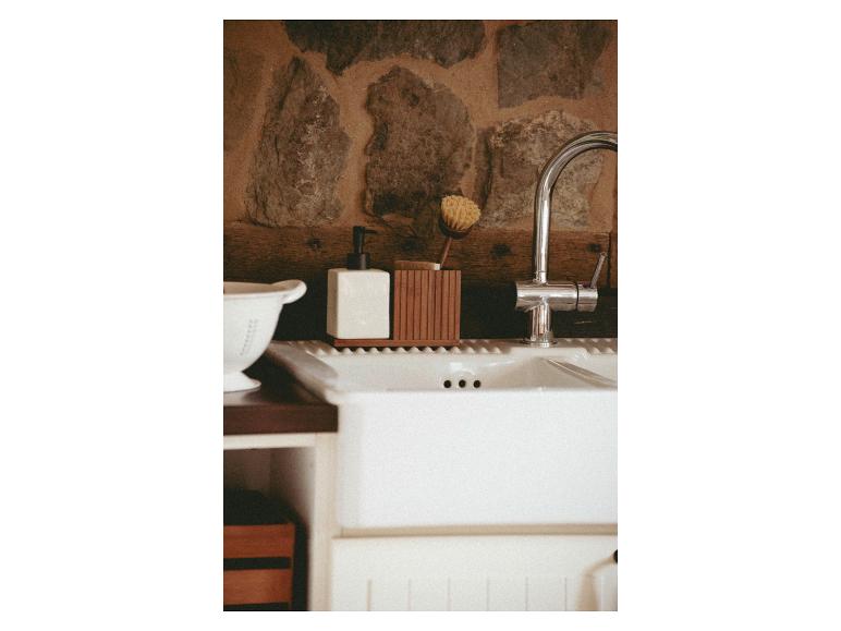 Ein weißer Keramik-Seifenspender und ein hölzerner Bürstenhalter stehen auf einem Küchenspülbecken.