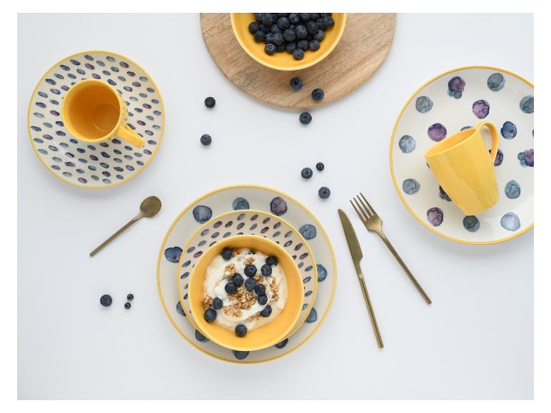 Frühstücksgedeck mit gelben Schalen und Tellern, Joghurt mit Blaubeeren und Müsli, sowie losen Blaubeeren.