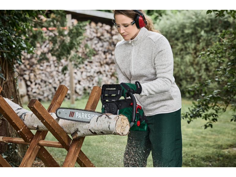 Frau benutzt eine Parkside Kettensäge, um Baumstämme auf einem Holzsägebock zu schneiden.