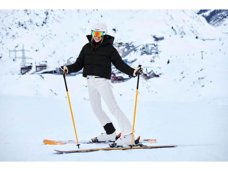 Eine Frau in schwarzer Skijacke und weißer Hose fährt Ski auf einer verschneiten Piste.