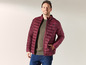 Mann in einer dunkelroten Daunenjacke und Jeans.