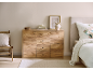 Holzkommode in einem Schlafzimmer mit Bett und Stuhl.