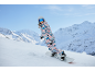 Frau in farbenfrohem Snowboardanzug und Helm fährt Snowboard in den Bergen.