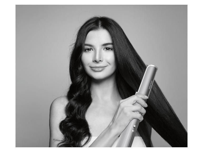 Frau stylt ihr langes Haar mit einem Glätteisen, halb glatt, halb lockig.