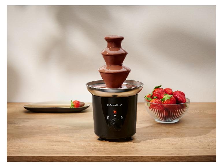 Schwarzer Schokoladenbrunnen mit frischen Erdbeeren auf einem Holztisch.