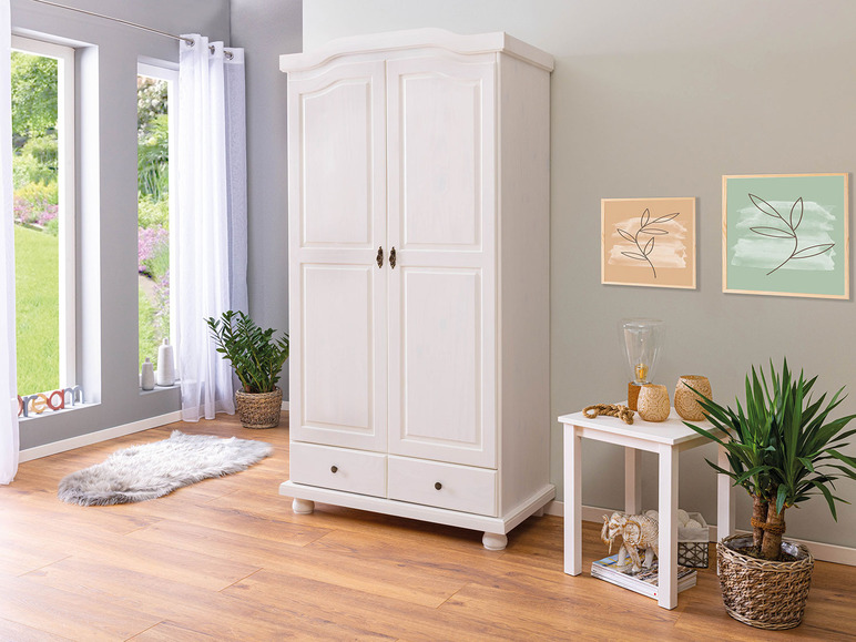 Ein weißer Kleiderschrank mit zwei Türen und einer Schublade in einem modernen Wohnzimmer.