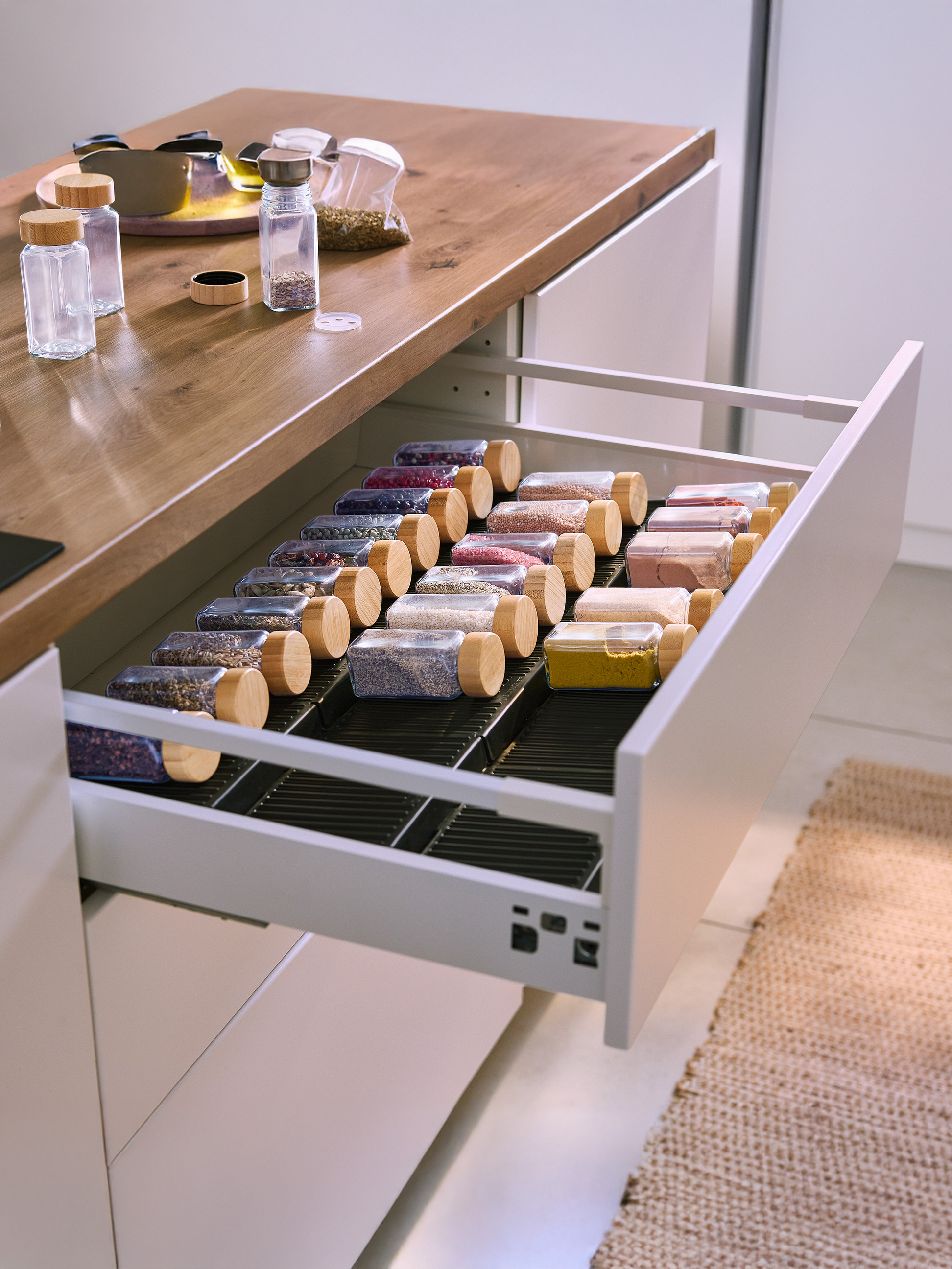 Offene Küchenschublade mit Glas- und Holzgewürzgläsern, gefüllt mit bunten Gewürzen.