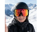 Frau mit schwarzem Skihelm und Skibrille mit reflektierenden Gläsern vor verschneiten Bergen.