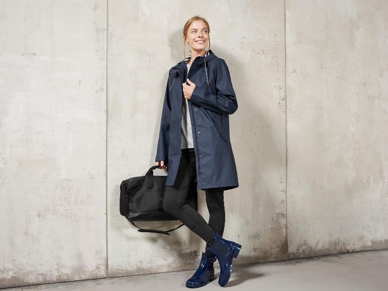 Eine Frau trägt einen blauen Regenmantel, eine schwarze Tasche und blaue Gummistiefel.