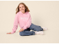 Mädchen in rosa Hoodie mit 'ASPEN COLORADO'-Aufdruck und Jeans sitzt lächelnd
