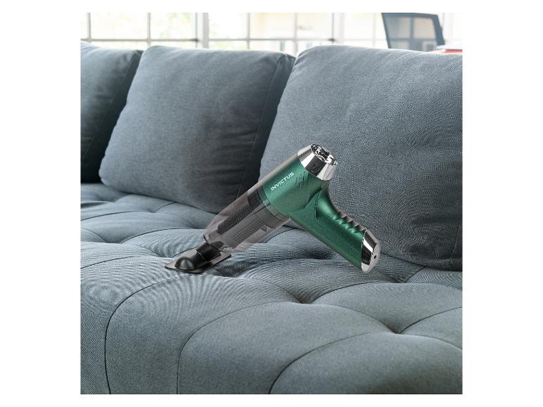 Grüner Invictus Handstaubsauger reinigt ein graues Sofa.