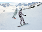 Zwei Snowboarder in Skikleidung fahren einen verschneiten Hang hinunter, Berge im Hintergrund.