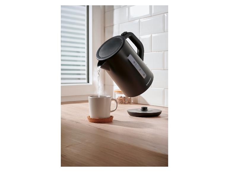 Schwarzer Silvercrest Wasserkocher gießt heißes Wasser in eine weiße Tasse auf einer Holzküchenarbeitsplatte.