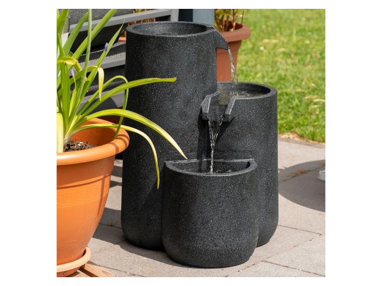 Gestufter Wasserspiel mit fließendem Wasser, neben einer Topfpflanze auf einer Terrasse.