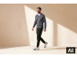 Lächelnder Mann geht, trägt einen grauen V-Pullover, schwarze Hosen und weiß-blaue Sneaker.