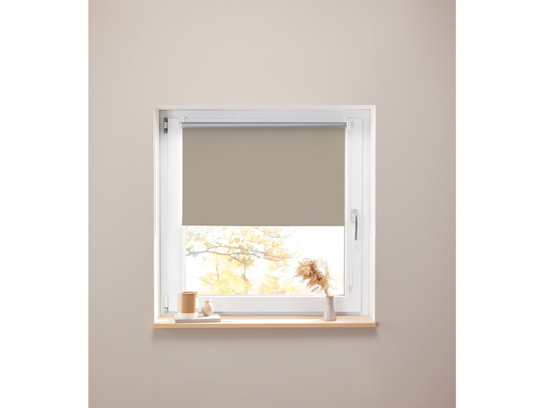 Ein beigefarbenes Rollrollo an einem Fenster mit einer Holzfensterbank.