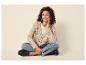 Frau in beiger Strickjacke, Jeans und schwarzen Loafern sitzt im Schneidersitz.