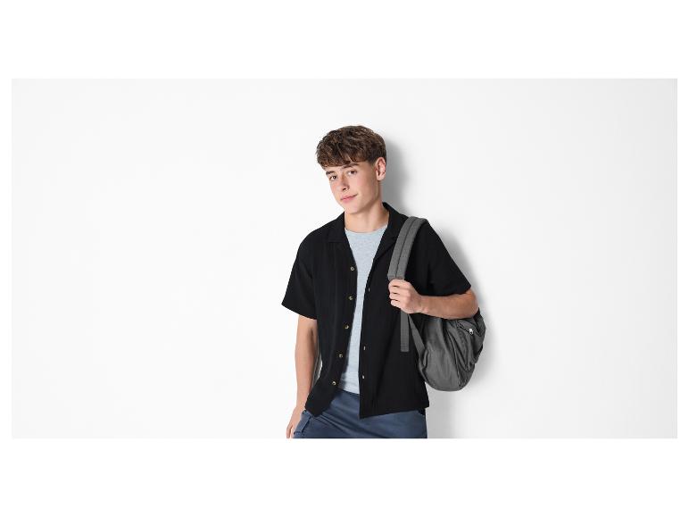 Junger Mann in schwarzem Hemd, grauem T-Shirt und Rucksack.