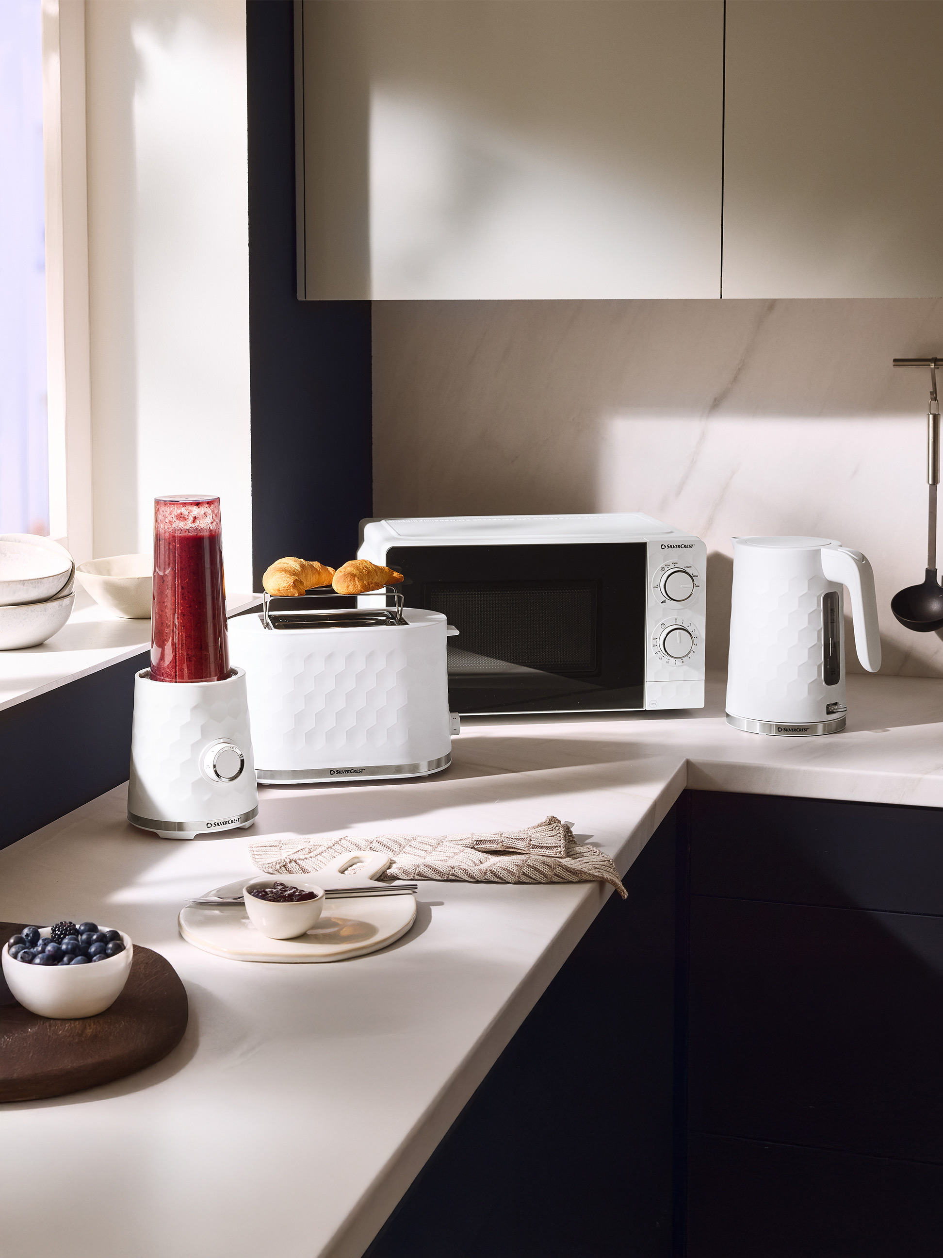 Weiße Küchengeräte: Mixer, Toaster mit Croissants, Mikrowelle und Wasserkocher.