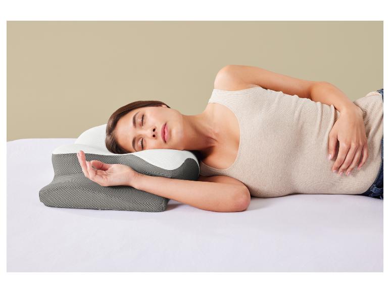 Frau schläft auf der Seite auf einem Bett mit einem grau-weißen ergonomischen Kissen.