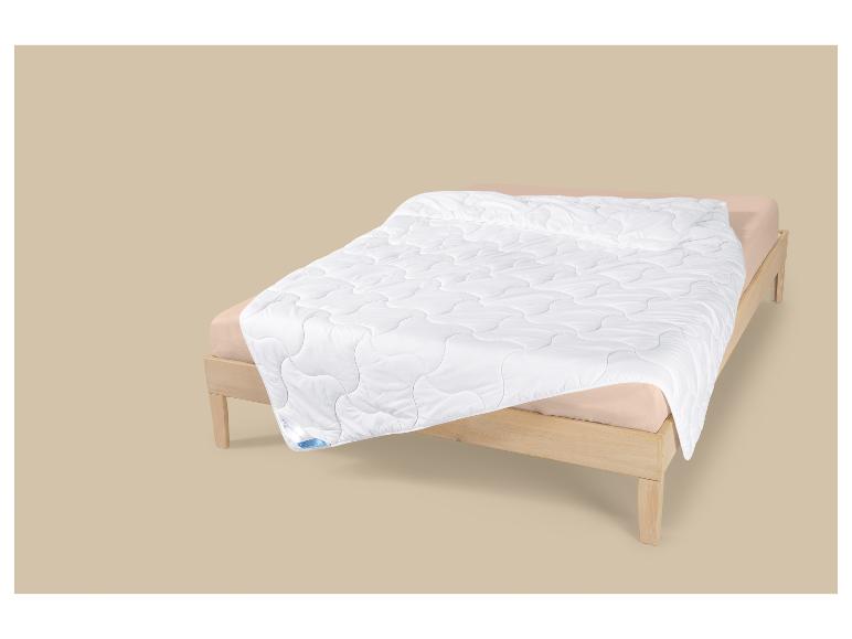 Weiße Steppdecke mit Wellenmuster auf einem Holzbett mit beigefarbener Bettwäsche