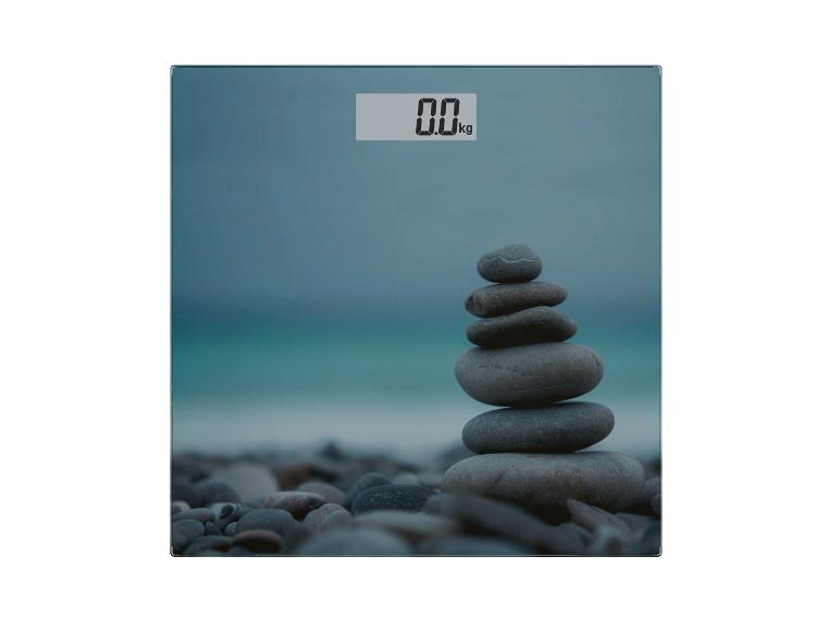 Digitale Personenwaage mit 0.0 kg Anzeige und gestapelten Steinen am Strand.