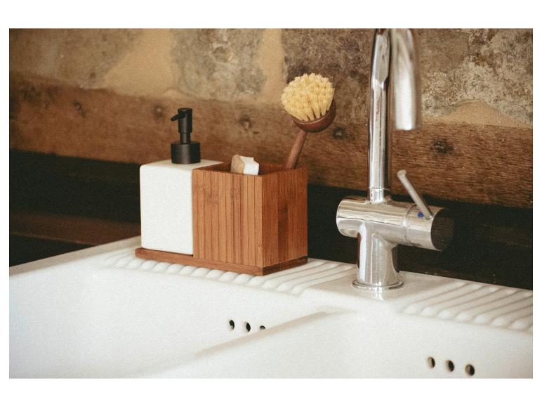 Spülmittelspender und Spülbürste in einem Bambus-Organizer in einer rustikalen Küche.