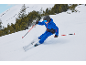 Kind fährt Ski in blauem Skianzug, mit Skiern, Stöcken, Helm und Brille auf verschneitem Berg.