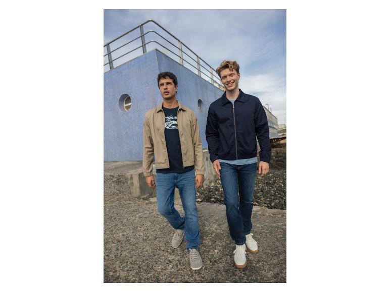 Zwei Männer in Jeans und Jacken, die an einem blauen Gebäude vorbeigehen.