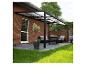 Schwarze Pergola mit transparentem Dach über einer Terrasse mit Gartenmöbeln und Pflanzen.