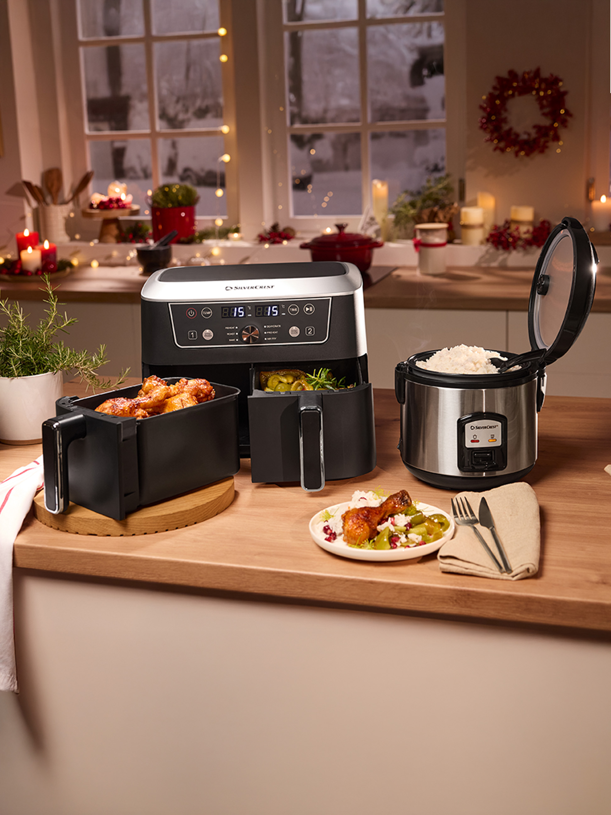 Silvercrest Heißluftfritteuse und Reiskocher auf einer Küchenarbeitsplatte, mit gekochtem Essen und festlicher Dekoration.