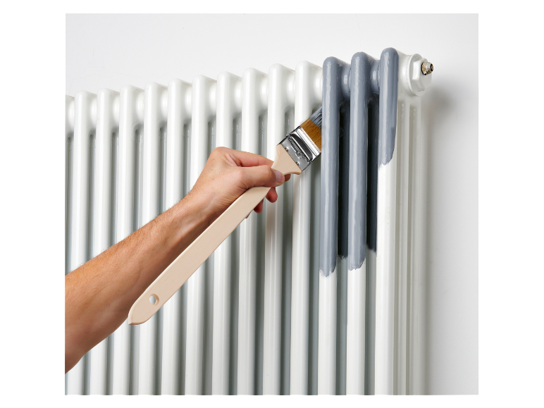 Eine Person streicht einen Heizkörper grau.