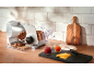 Brotschneidemaschine mit geschnittenem Brot, Marmelade und Käse auf einer Holztheke.