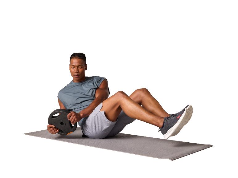 Mann trainiert mit einer Hantelscheibe auf einer Yogamatte.