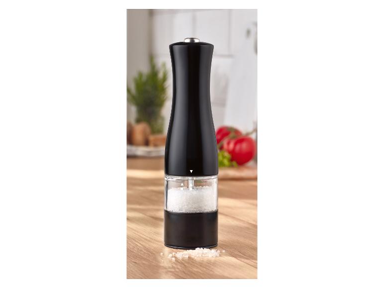 Schwarze Salz- oder Pfeffermühle auf einem Holztisch mit Tomaten im Hintergrund.
