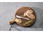 Holzbrett mit geschnittenem Brot, Kräuterbutter, einem Buttermesser und frischen Kräutern.
