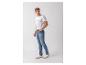Mann in weißem bedrucktem T-Shirt und blauen Jeans, mit der Hand in der Tasche.